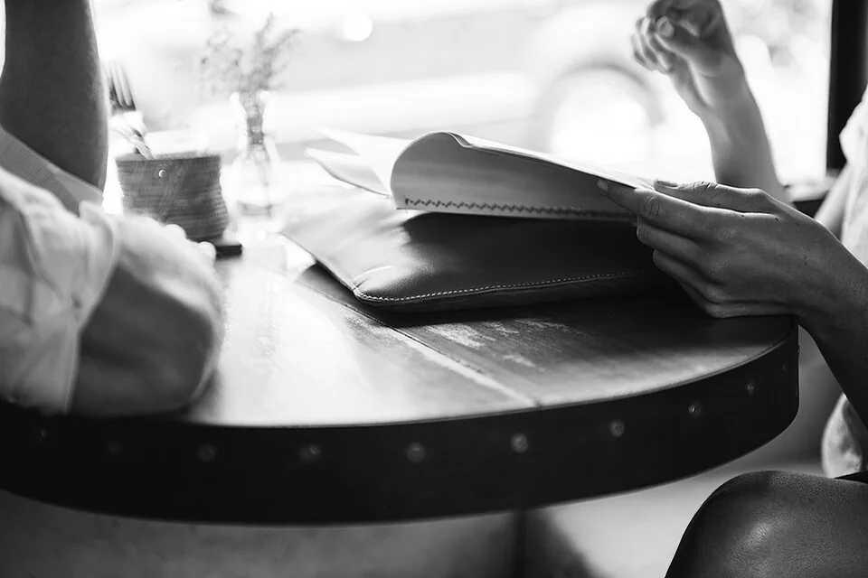 A black-and-white close view of hands holding an open notebook at a cafe table.