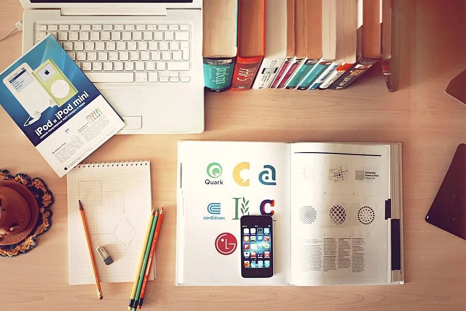 Laptop, phone, notebooks and books arranged on a wooden desk.